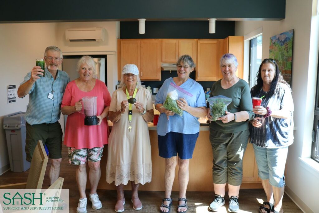 A group of 6 residents of a SASH housing organization holding up smoothie ingredients.